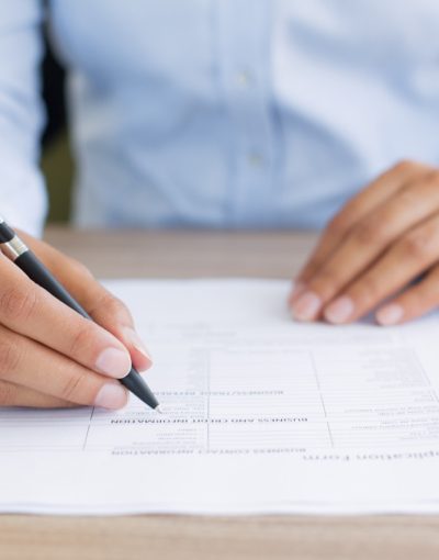 Cropped view of person holding pen and filling out application form on table